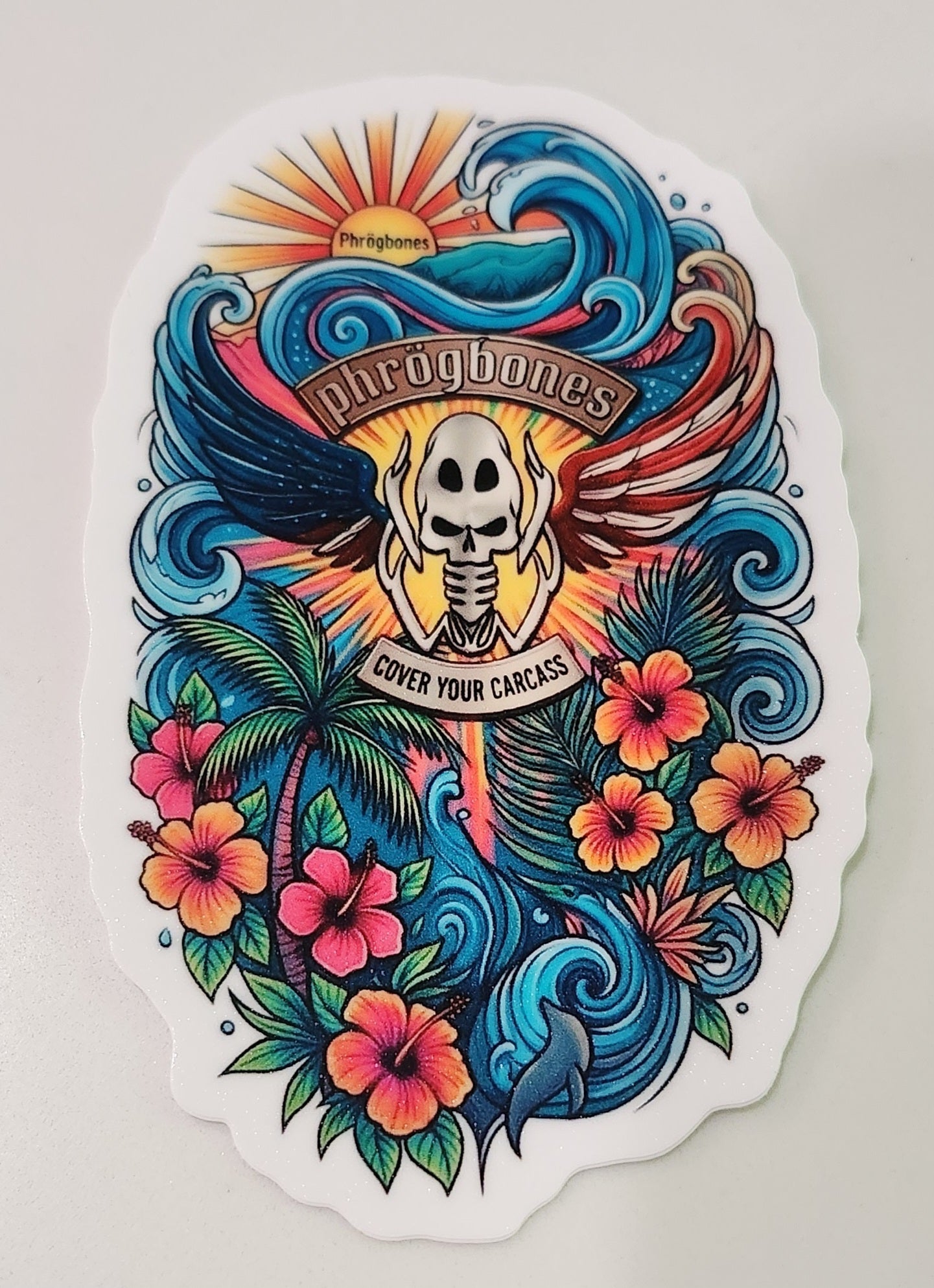 A die-cut vinyl sticker featuring a colorful tattoo-style illustration of a Phrogskull, waves, tropical flowers, and the text 'Phrogbones' and 'Cover Your Carcass' on a white background.
